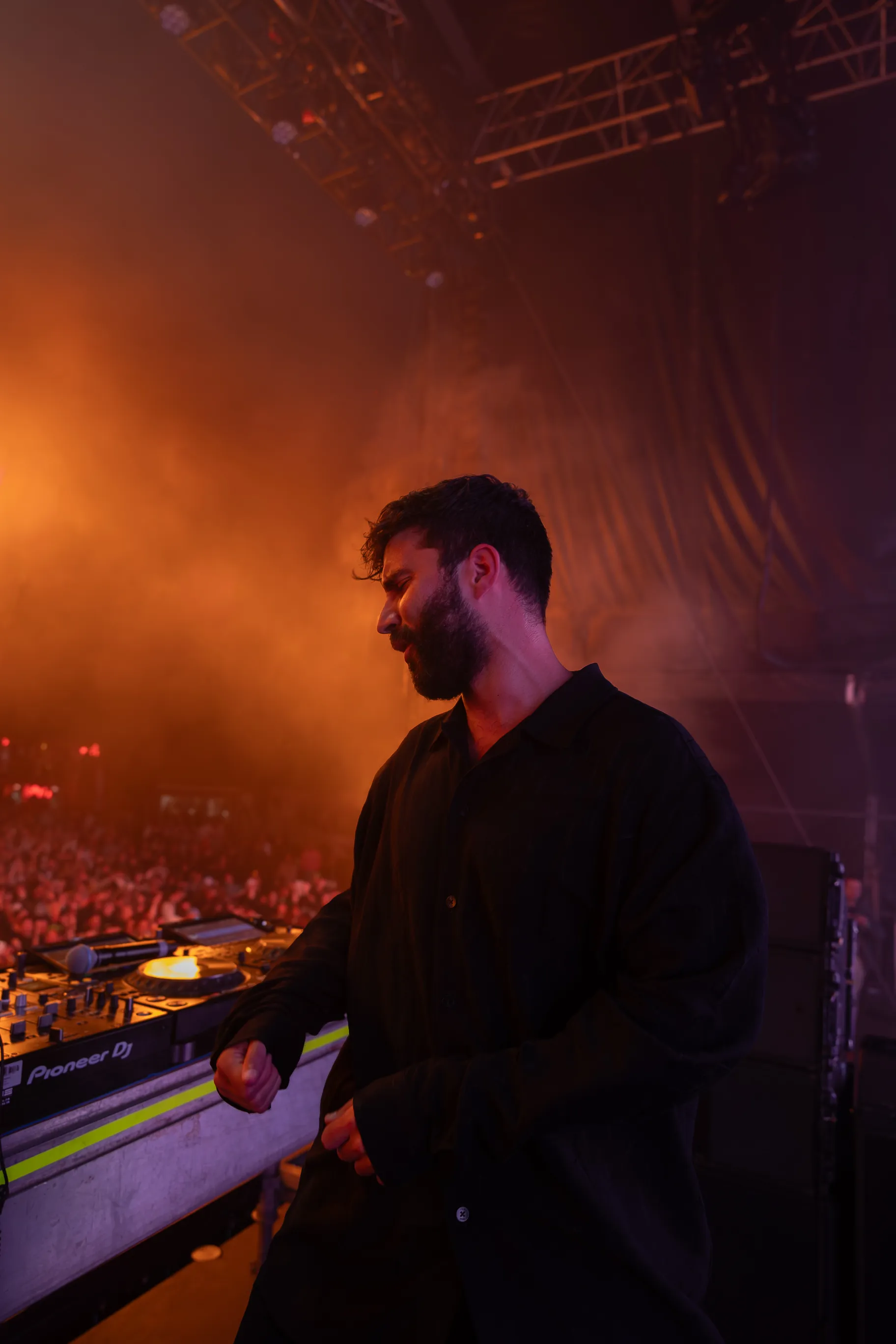 A DJ performing behind a DJ deck, with the crowd visible in the background