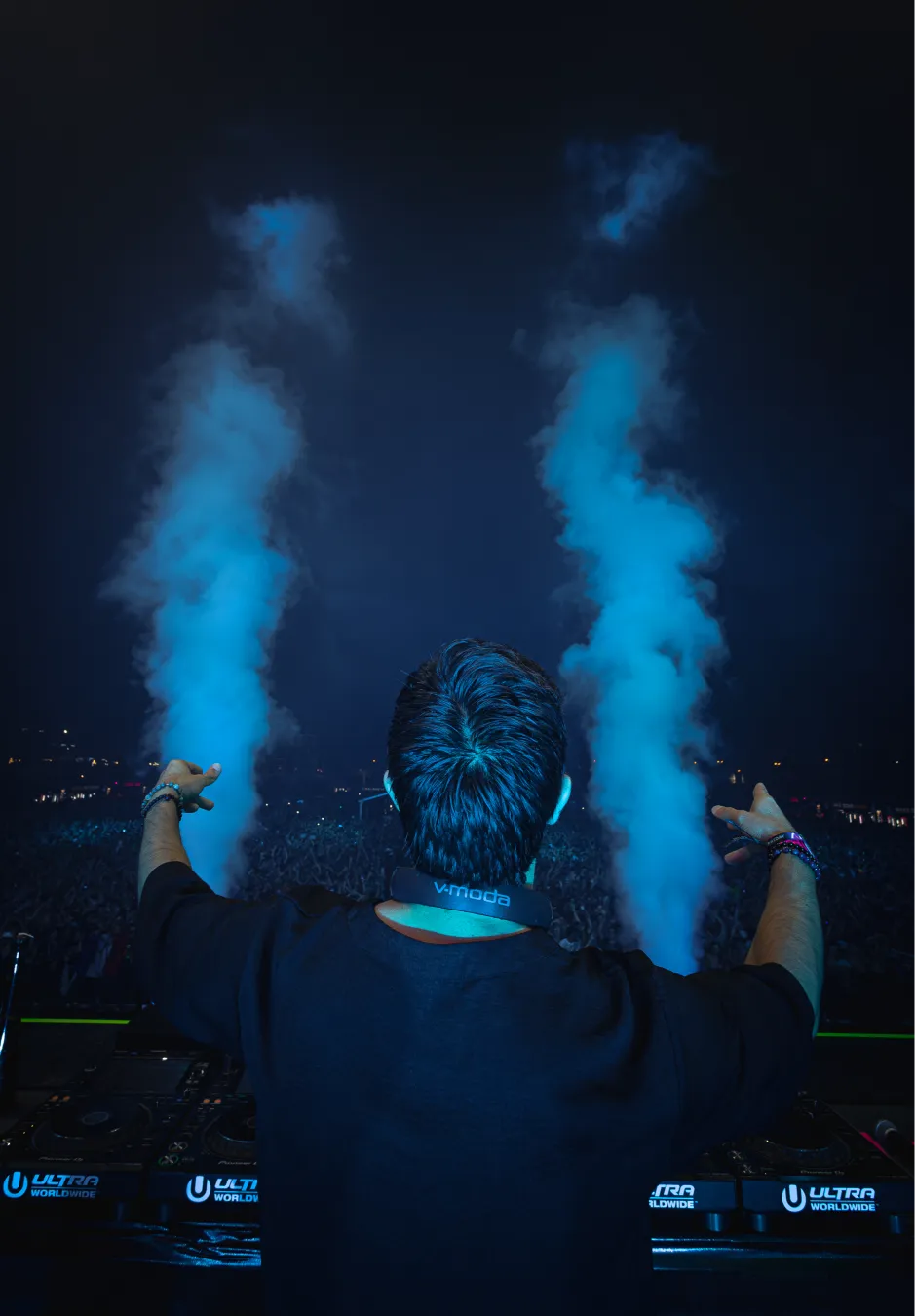 A DJ raises his hands, facing the crowd